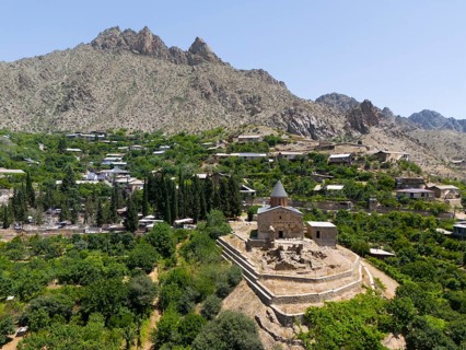 Small historic church on a hill with mountains in the background and lush vegetation, aerial view,