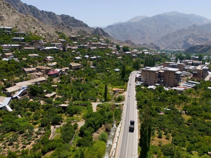 Village with a road winding through a mountainous landscape with green vegetation, aerial view,