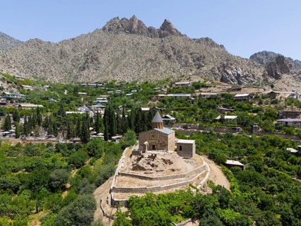 Historic mountain church surrounded by lush vegetation and impressive mountains, aerial view, St