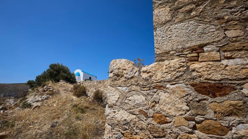 Stone wall in the foreground with blue roof in the background under a clear sky, Panagia tou