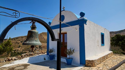 Small white-blue chapel in the countryside with bell in the foreground and blue sky in the
