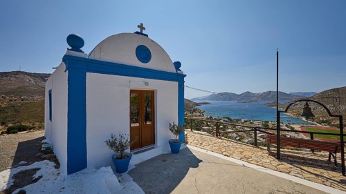 White-blue chapel with a view of a hilly landscape and the sea in the background, Panagia tou
