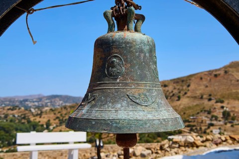 Antique metal bell in rural setting with background landscape and blue sky, Panagia tou