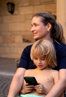 Mother, woman, has boy, 6 years, blonde, in arms, playing with smartphone, mobile phone, upper body