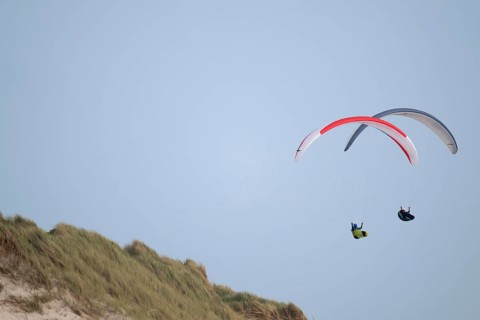 Two paragliders or paragliders in front of a blue sky over a dune landscape, near Hvide Sande,
