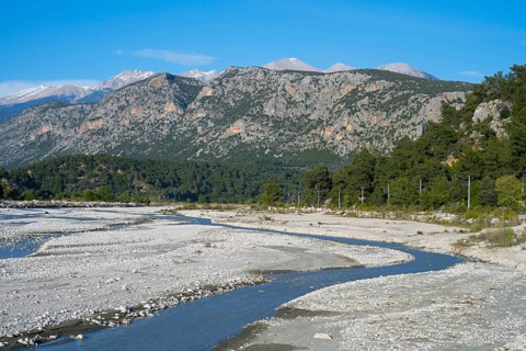 A calm river flows through a wide gravel bed, framed by forested mountains, Dargaz River near