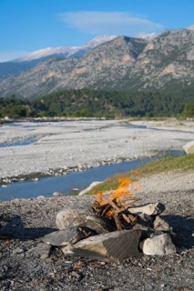 A campfire in a rocky landscape with mountains and a riverbed in the background, Dargaz River near