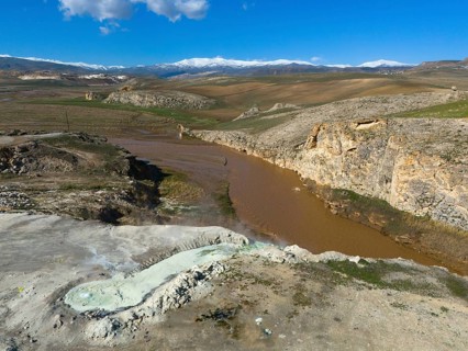 Vast landscape with brown river and rocky gorge under blue sky and white clouds, aerial view,
