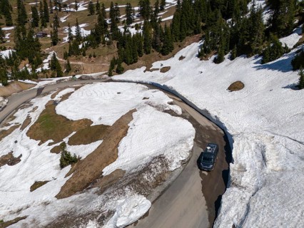 Bird's eye view of a car on a snowy mountain road with curves and fir trees, aerial view, camper,