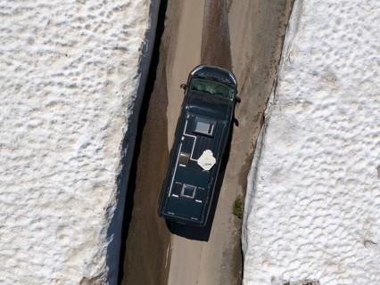 Car driving between high snow walls on a narrow road, seen from above, aerial view, camper,