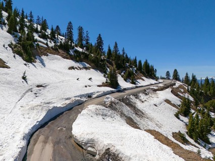 Snowy mountain road with serpentines and fir trees under a clear blue sky, aerial view, near