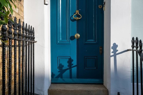 Blue door with brass-coloured door handle and wrought-iron grille in the sunlight, Kensington,