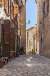 A narrow alley in a quiet village with old buildings and open shutters, Aurel, Département