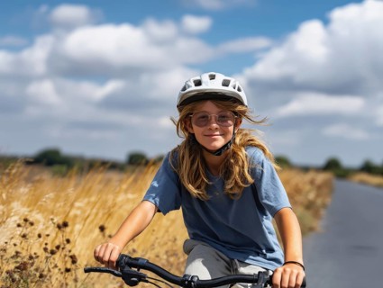 A girl with a bicycle helmet rides a bicycle and smiles friendly into the camera, AI generated, AI