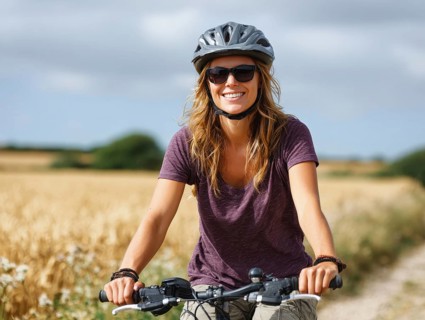 A young woman with a bicycle helmet rides a bicycle and smiles friendly into the camera, AI