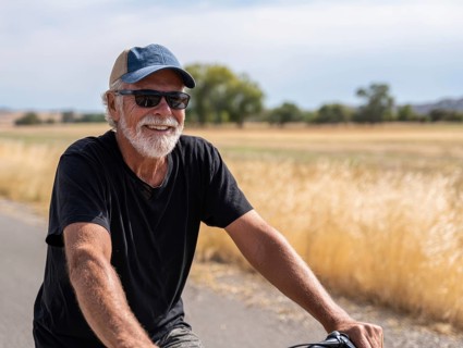 A man, senior citizen rides a bicycle and smiles friendly into the camera, AI generated, AI