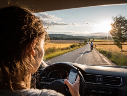 A car driver is dazzled by the sun and looks at her smartphone while driving, putting herself, the