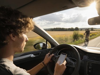 A car driver is dazzled by the sun and looks at his smartphone while driving, putting himself, the