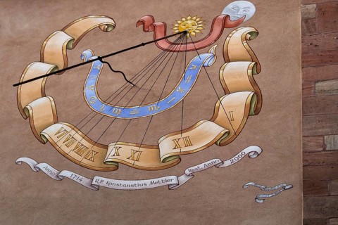 Artfully painted sundial on a sandstone wall with Roman numerals and decorative elements, Alsace,