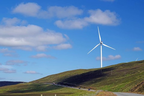 Single wind turbine on a hill next to a road under a blue sky, Mainland, Shetland Islands,