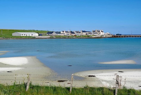 Coastline with sand and village by the shimmering blue sea, Pierowal, Westray, Orkney Islands,