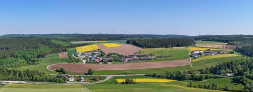 Far-reaching panoramic view of a village with surrounding fields and wind turbines, near
