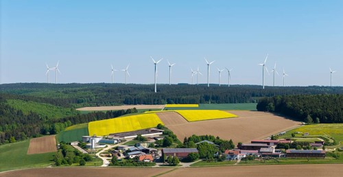 Idyllic landscape with wind turbines and blossoming rape fields in a small village, near