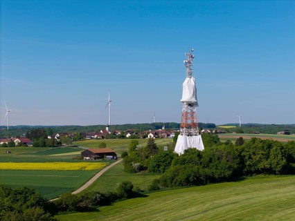 A transmission tower and wind turbines near a village under a blue sky, radio tower being