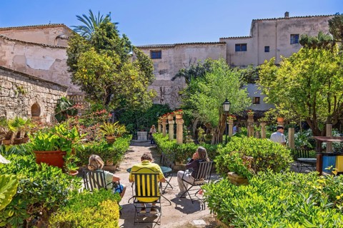 People sitting on chairs and enjoying the sun in the botanical garden at The Arab baths in Palma,