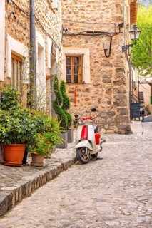 Scooter standing outside a house on the city street with lush green plants in pots on the pavement