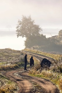 Two people walking on a winding gravel road in the countryside on a foggy autumn day
