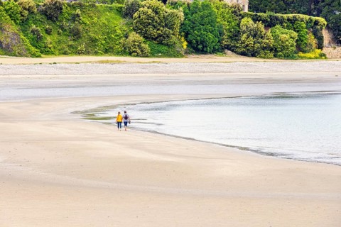Two people walking at the waters edge on a sandy beach by the sea, Morgat, Crozon peninsula,