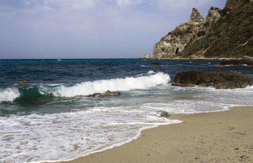 Waves rolling over the sandy beach, rocky coast in the distance, Ricadi, Capo Vaticano