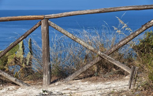 Rustic wooden fence overlooking the blue sea and coastal vegetation, Ricadi, Capo Vaticano
