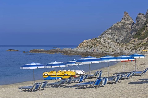 Beach with sunbeds and parasols in front of a rocky coast and blue sky, Ricadi, Capo Vaticano