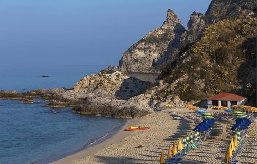 Quiet beach with parasols in front of a rocky coast and blue sea, Ricadi, Capo Vaticano