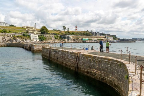 Fishing from harbour wall, seafront coastline waterfront, Plymouth, Devon, England, UK view east to