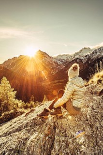 Woman sitting thoughtfully at a feslen at autumn atmosphere during sunset in the Swiss Alps in the