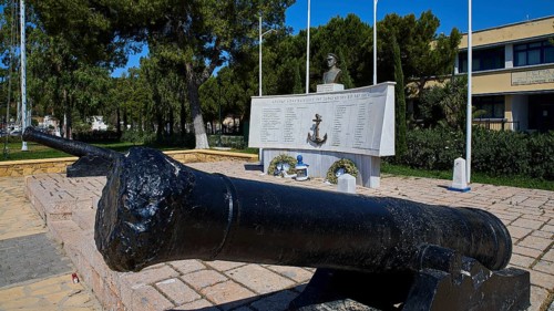 A monument with cannons and bust, surrounded by inscriptions and green vegetation in the open,