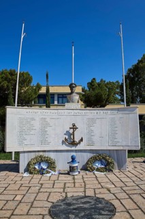 An open-air monument with bust and anchor, accompanied by plaques with inscriptions and wreaths,