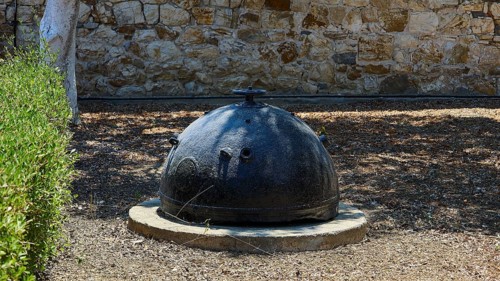 Bellini's Tower, Museum, An old black mine sits on a concrete foundation in front of a stone wall,