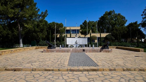 WW2, A memorial with cannons and flags stands on a paved square surrounded by trees, photos