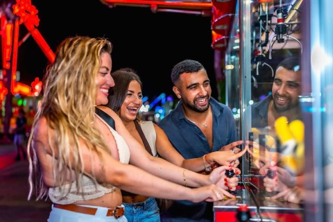 Happy friends enjoying a night out at amusement park, playing skill crane game and trying to win a