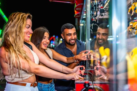 Group of friends having fun playing a crane game, trying to grab a prize, at an amusement park at