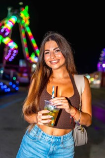Young woman holding a refreshing cocktail at an amusement park, enjoying the vibrant night