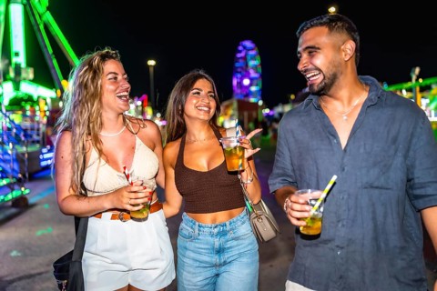 Three joyful friends walking and laughing together at an amusement park at night, enjoying colorful