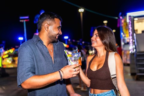 Young man and woman smiling and toasting with colorful cocktails while enjoying the vibrant