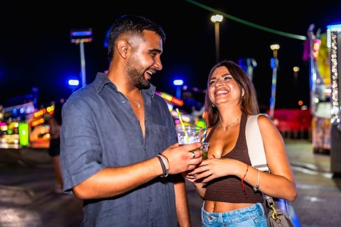 Young man and woman laughing joyfully while enjoying cocktails together, surrounded by the vibrant
