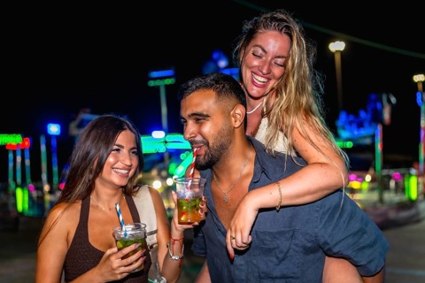 Group of cheerful friends enjoying cocktails and laughing together at an amusement park during a