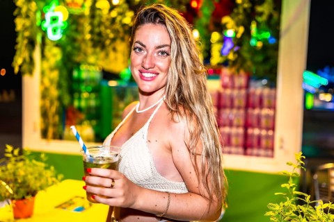 Young woman smiling and holding a refreshing cocktail at a vibrant night market, enjoying the